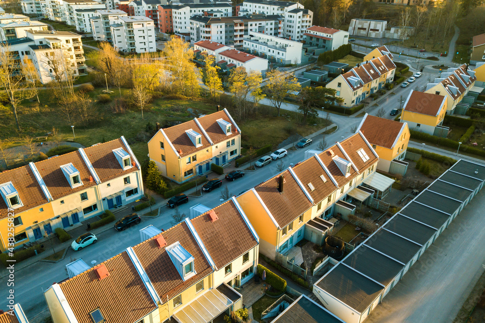 Fototapeta premium Aerial view of residential houses with red roofs and streets with parked cars in rural town area. Quiet suburbs of a modern european city.