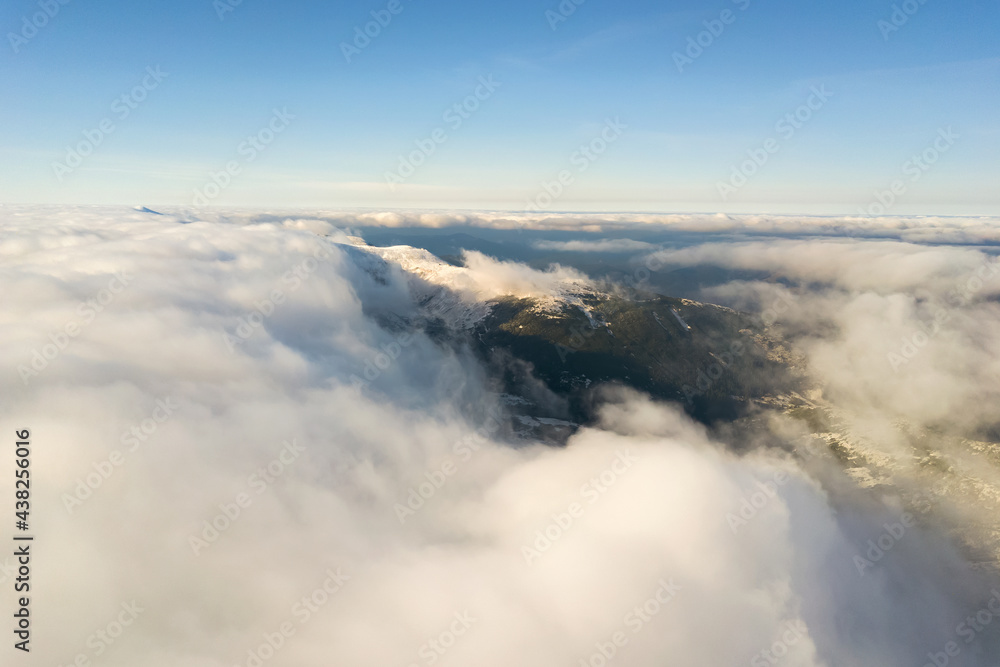 Aerial view from above of white puffy clouds covering snowy mountain tops in bright sunny day. Aerial view from above of white puffy clouds covering snowy mountain tops in bright sunny day.