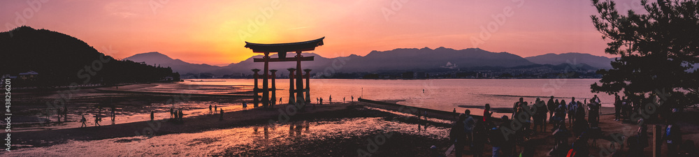 Amazing super wide panorama view of torii gate and sunset with travelers over the sea with mountains in the horizon from the Miyajima Island, Japan