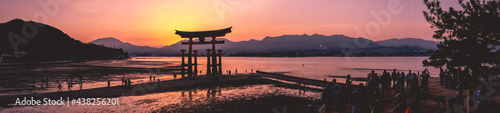 Amazing super wide panorama view of torii gate and sunset with travelers over the sea with mountains in the horizon from the Miyajima Island, Japan