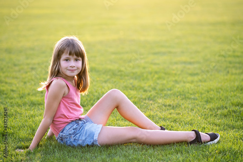 Young pretty child girl laying down on green grass lawn on warm summer day. © bilanol