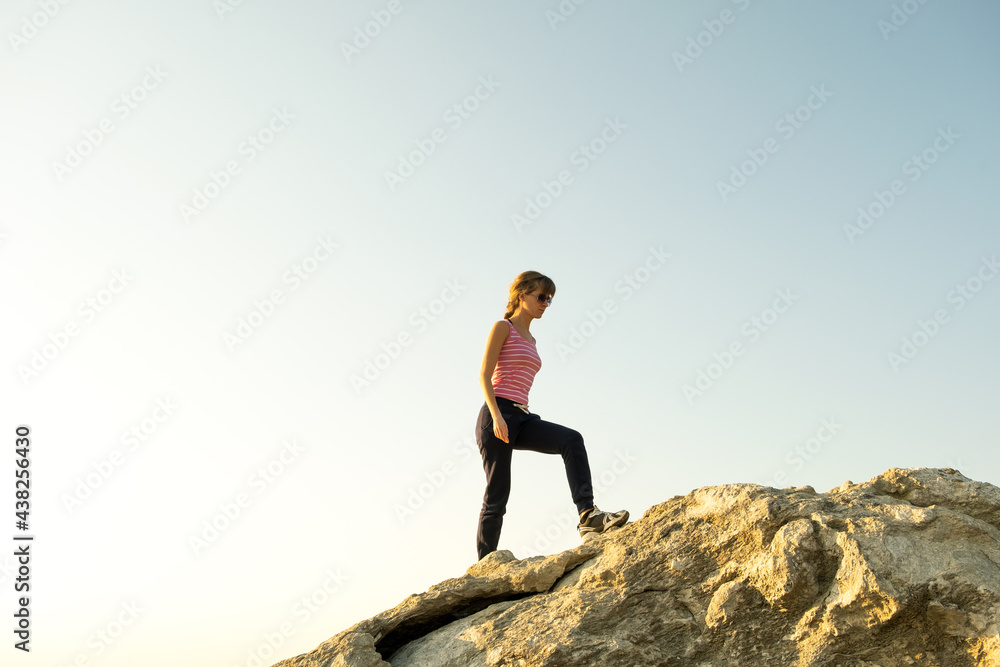 Woman hiker climbing steep big rock on a sunny day. Young female climber overcomes difficult climbing route. Active recreation in nature concept. Woman hiker climbing steep big rock on a sunny day. Young female climber overcomes difficult climbing route. Active recreation in nature concept.