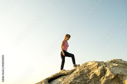 Woman hiker climbing steep big rock on a sunny day. Young female climber overcomes difficult climbing route. Active recreation in nature concept.