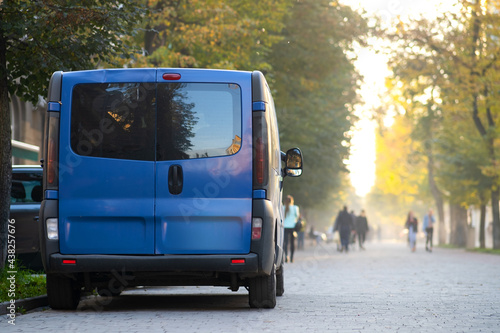 Passenger van car parked on a city alley street side with blurred walking pedestrians in autumn.