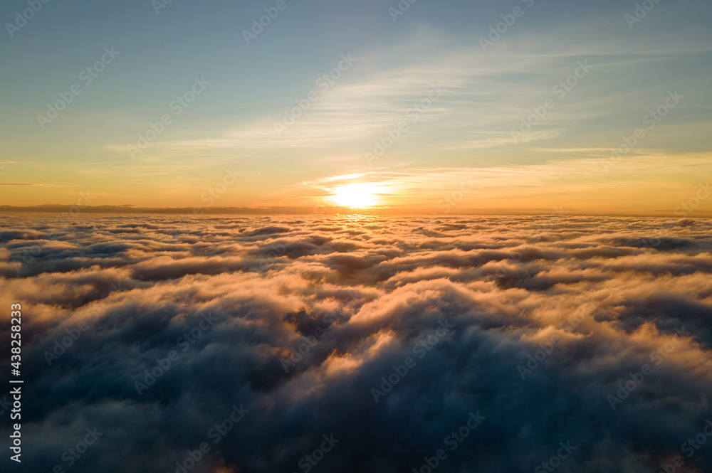 Aerial view of vibrant yellow sunrise over white dense clouds with blue sky overhead.