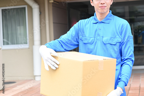 屋外で作業服を着た男性が引っ越しの段ボールを運ぶイメージ  © koumaru