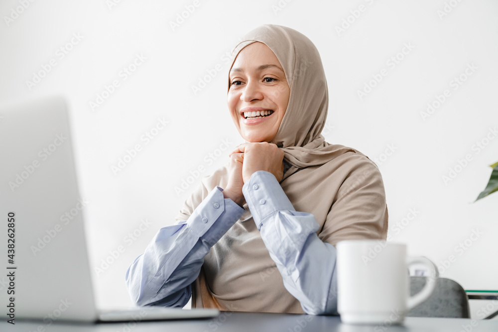 Happy mature arabian islamic muslim businesswoman in hijab watching webinars, online classes, movies and e-learning. Remote work. Lockdown concept Happy mature arabian islamic muslim businesswoman in hijab watching webinars, online classes, movies and e-learning. Remote work. Lockdown concept