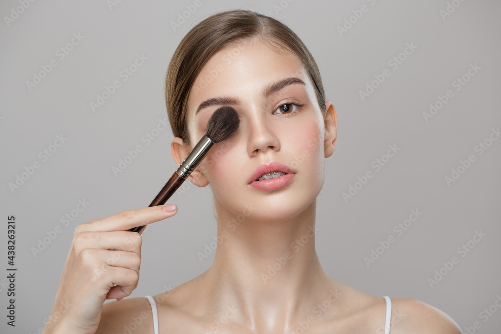 Obraz premium Portrait of a girl with perfect skin holding a makeup brush. Gray background.