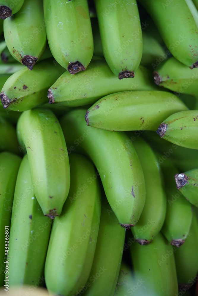 Many green bananas in a pile at market. Close-up texture of a stack of unripe bananas.