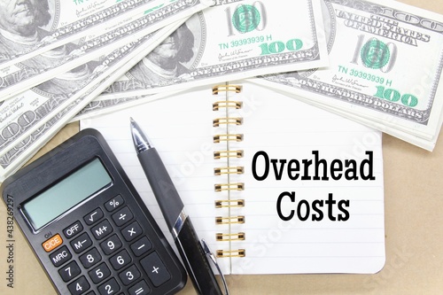 notebooks, pens, calculators, banknotes with the word overhead costs photo