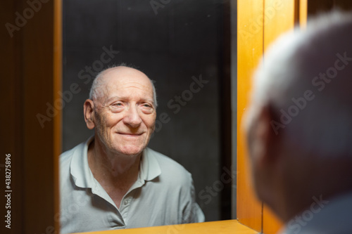 Old man looking happy and smiling at his reflection in front of a mirror in the bathroom