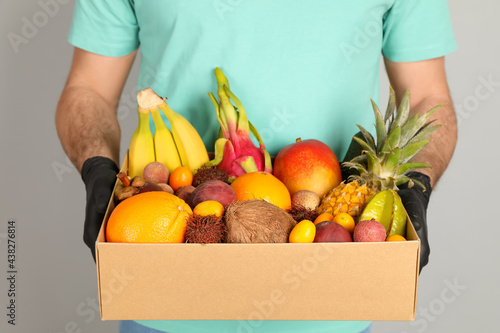 Fototapeta Naklejka Na Ścianę i Meble -  Courier holding box with assortment of exotic fruits on grey background, closeup