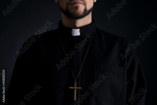 Priest wearing cassock with clerical collar on dark background, closeup photo