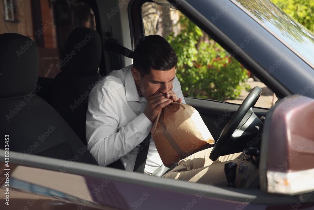 Man with paper bag suffering from nausea in car Man with paper bag suffering from nausea in car