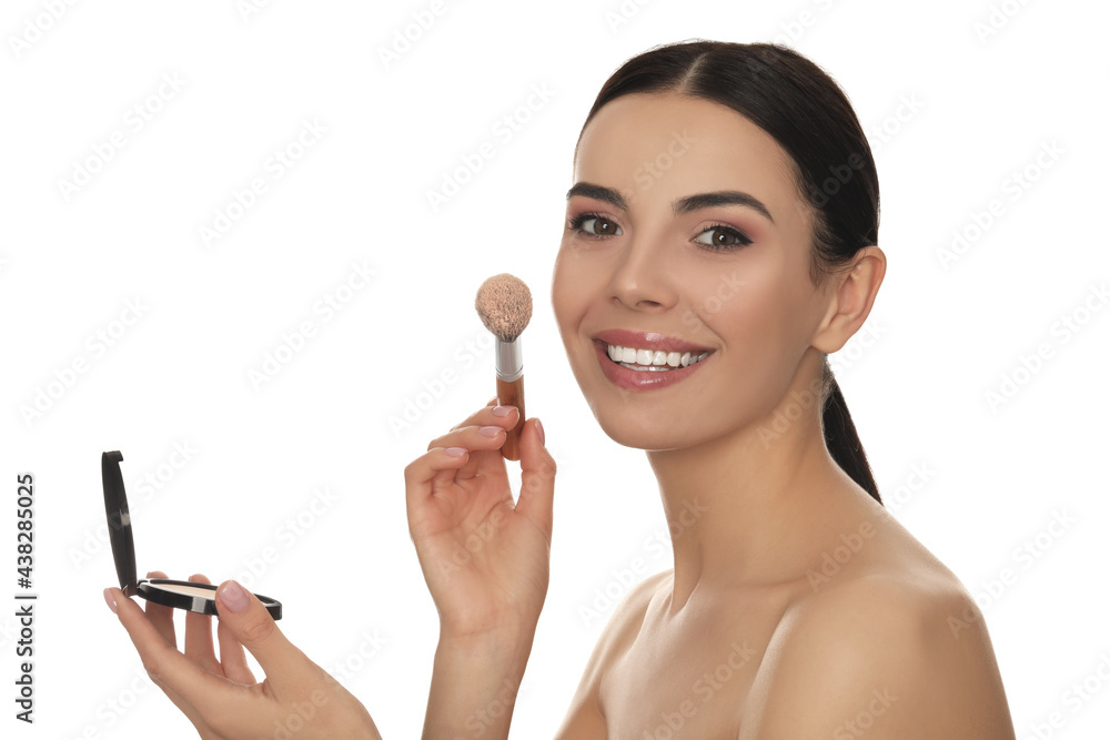Beautiful young woman applying face powder with brush on white background