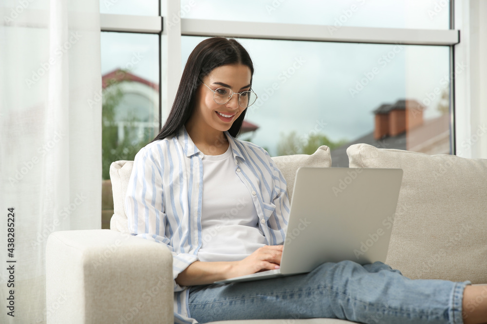Fototapeta premium Young woman with laptop on sofa at home