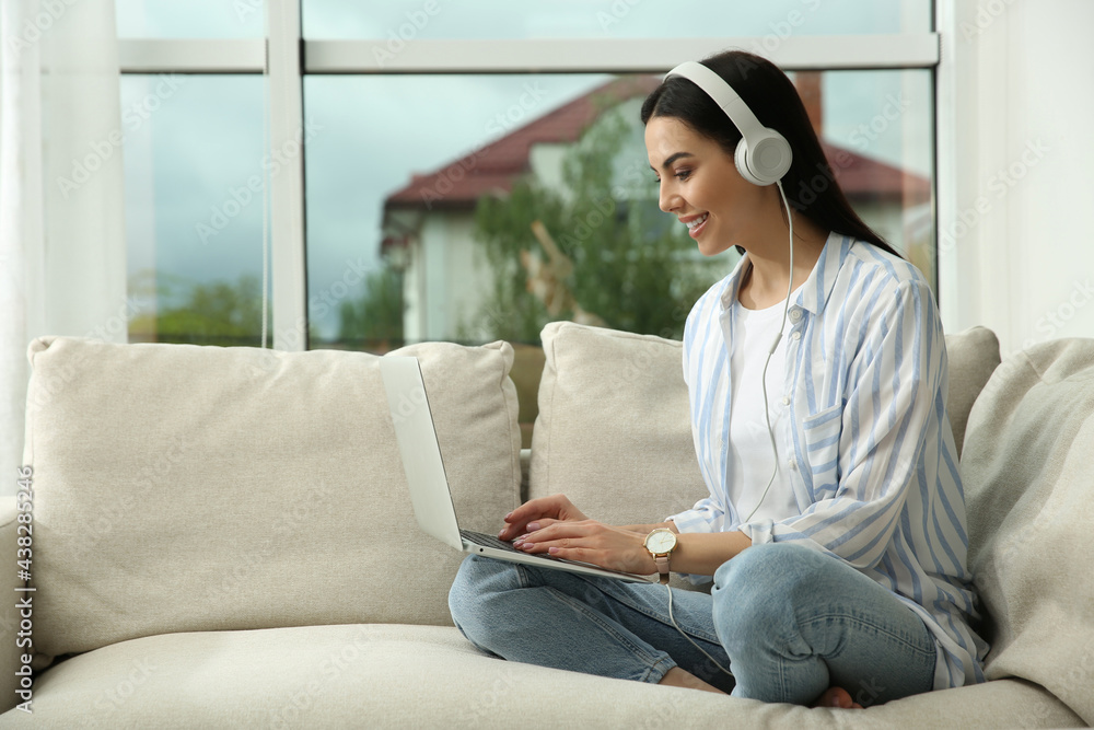 Young woman with laptop and headphones on sofa at home, space for text Young woman with laptop and headphones on sofa at home, space for text