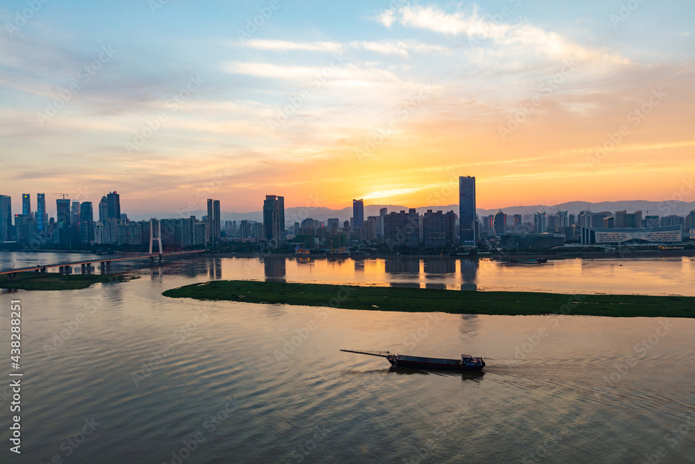 Nanchang, Jiangxi - June 8, 2021: In midsummer, the Ganjiang River is full of water, with ships passing by, tall buildings on both sides, and the city skyline is dazzled by the setting sun.