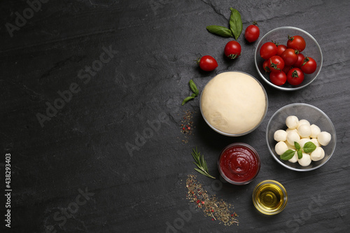 Raw pizza dough and other ingredients on black table, flat lay. Space for text