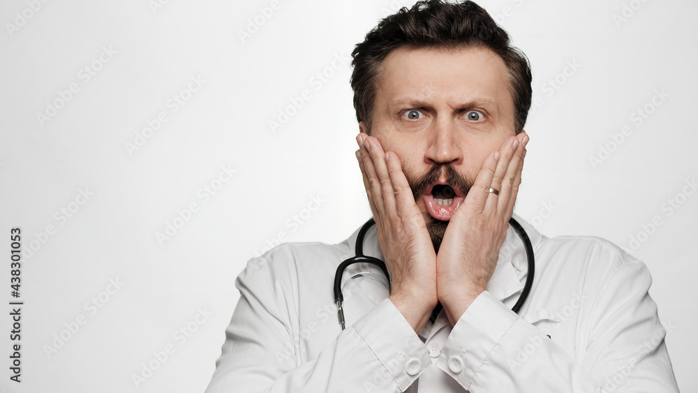 Doctor is surprised, shocked. Confused surprised man doctor on white background looking at camera and opens mouth and touches face with his hands