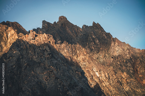 Scenic mountain landscape with great rocks in golden sunlight. Awesome rocky wall with sharp top in gold sunshine. Colorful sunny scenery with high rocky mountain with pointed pinnacle. Mountain wall.