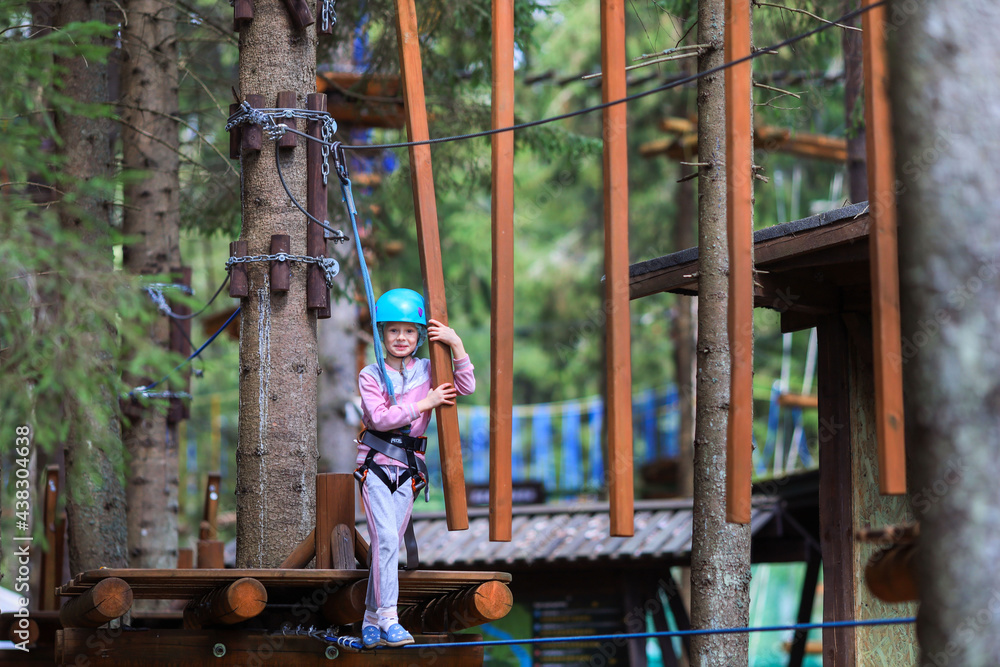 The child is engaged in sports.A girl overcomes sports obstacles in a rope park.A little girl in a protective helmet and tracksuit.Active recreation in the summer.Sports Rope Park for children