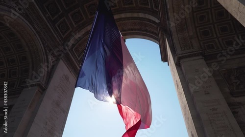 French flag flying in the wind under the Arc de Triomphe with the sun in the background - Paris, France