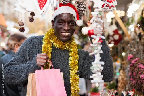 Portrait of African American in Santa hat looking happy with bags on Christmas market.