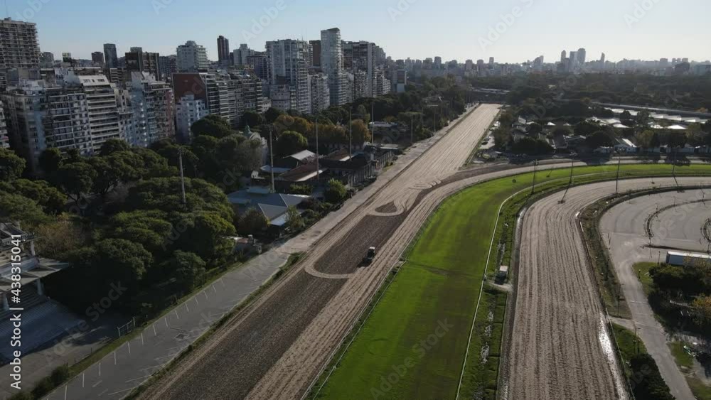 Aerial orbiting shot of tractor preparing racetrack for horse race in front of skyline in sunlight. Buenos Aires,Argentina Aerial orbiting shot of tractor preparing racetrack for horse race in front of skyline in sunlight. Buenos Aires,Argentina