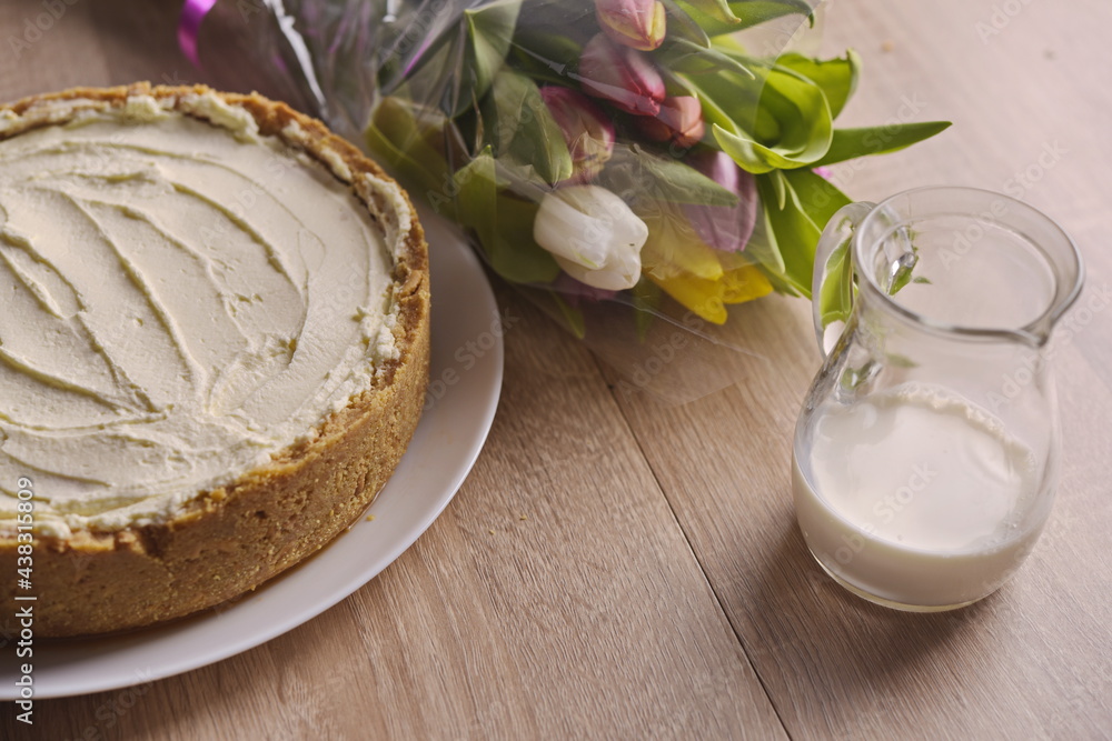 Banana homemade cake, a congratulatory bouquet of flowers and a jug of milk on the table. Banana homemade cake, a congratulatory bouquet of flowers and a jug of milk on the table.
