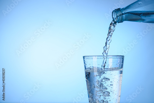 Pouring water from bottle into glass on color background