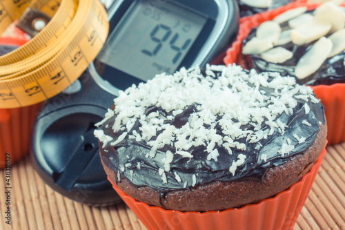 Glucometer with result sugar level, chocolate muffins and tape measure. Diabetes, slimming and dessert for different occasions
