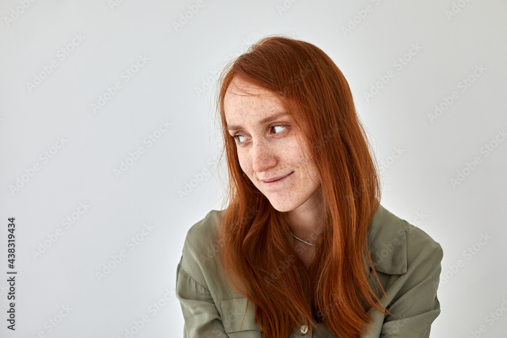 Obraz premium Timid female with long ginger hair and freckles smiling and looking away against white background