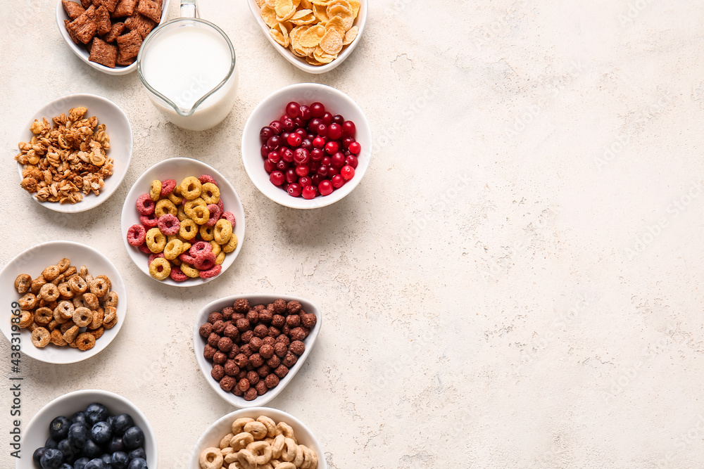 Bowls with different cereals, berries and milk on light background