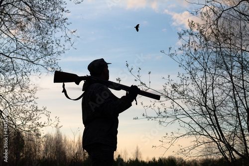 Photo a hunter with a rifle on his shoulder looks at a flying woodcock late at night