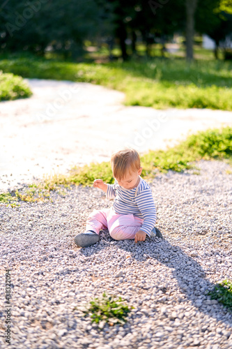 Little kid sitting on a gravel path in the park