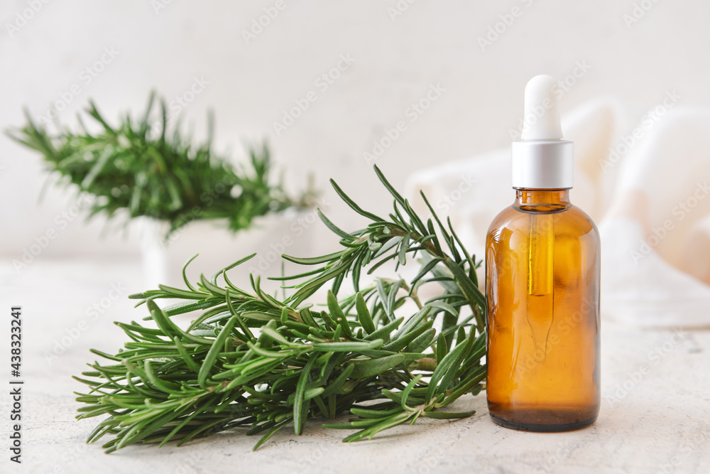 Bottle of essential oil and fresh rosemary on light background Bottle of essential oil and fresh rosemary on light background