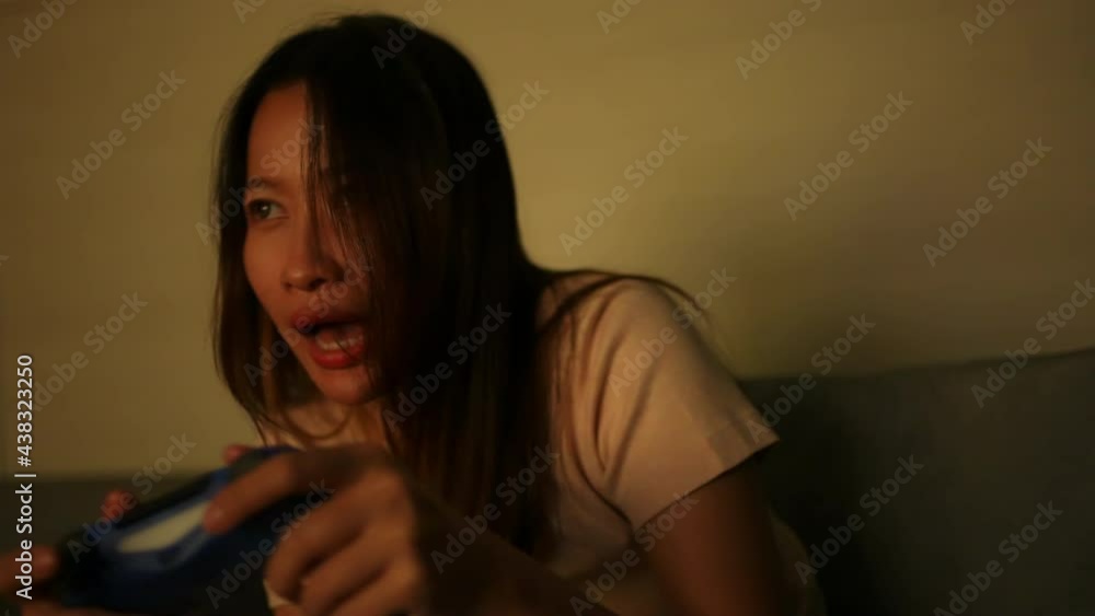Asian woman sitting on sofa holding game controller joystick playing video game with eating potato chip at night. Happy Female enjoy and having fun indoor lifestyle and hobby leisure game in apartment Asian woman sitting on sofa holding game controller joystick playing video game with eating potato chip at night. Happy Female enjoy and having fun indoor lifestyle and hobby leisure game in apartment