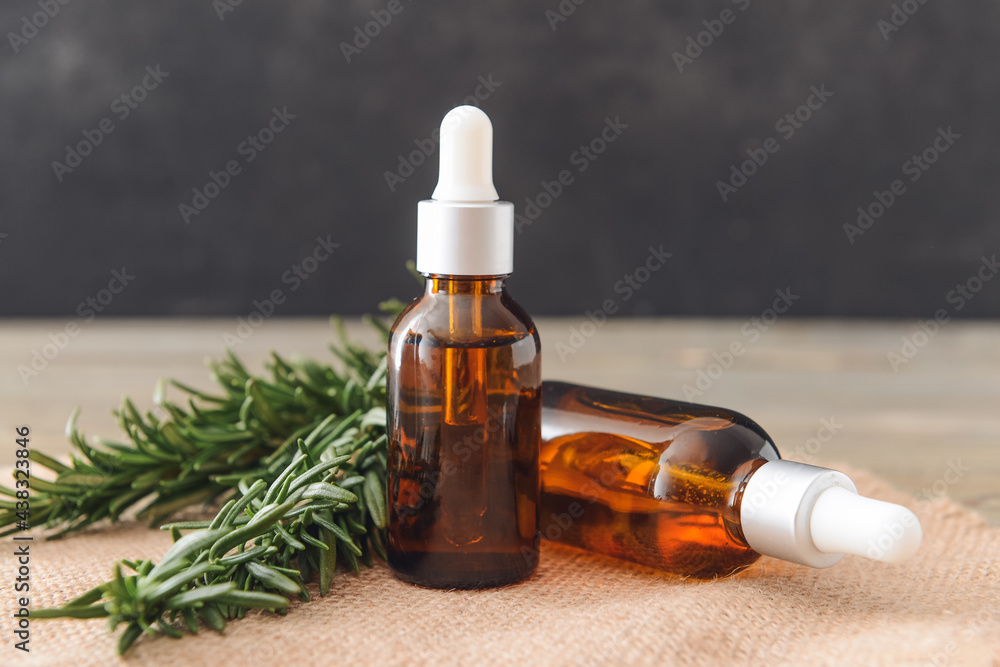 Bottles of essential oil and fresh rosemary on table Bottles of essential oil and fresh rosemary on table