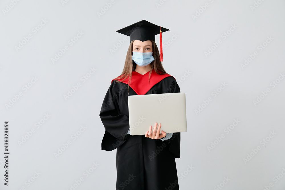 Female graduating student in protective mask and with laptop on light background Female graduating student in protective mask and with laptop on light background
