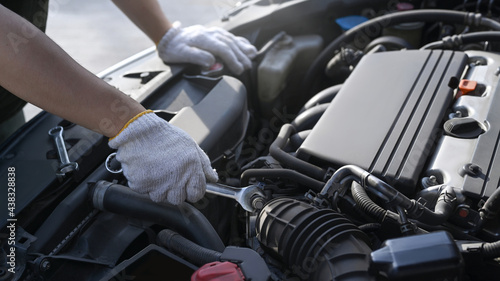 Cropped shot of auto mechanic using wrench repairing car at mechanics garage.