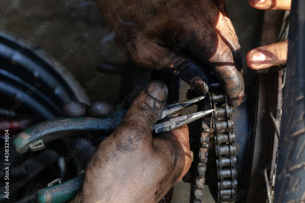 A middle aged man practicing a car in a car shop in Thailand is replacing a motorcycle chain.