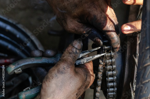 A middle aged man practicing a car in a car shop in Thailand is replacing a motorcycle chain. © kenmemoviey