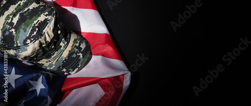 Military hat or bag laying with american flag. Soldier hat or helmet with national american flag on black background. Represent military concept by camouflage object and USA nation flag. photo