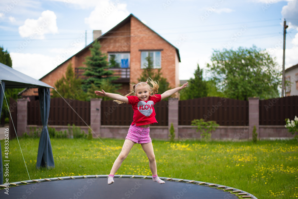 a cheerful child jumps on a trampoline on a warm day, in the courtyard of the house