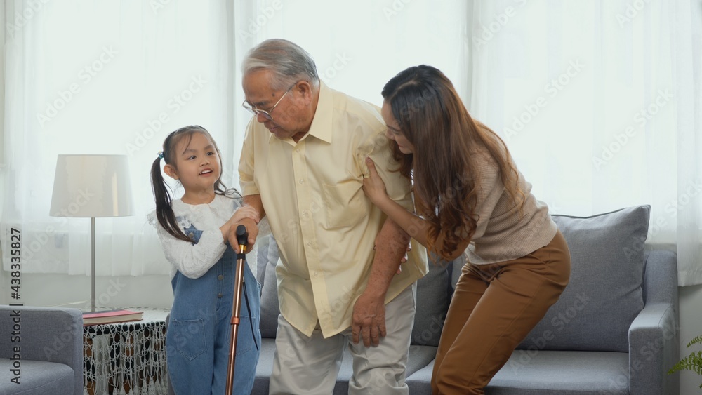 Fototapeta premium Asian family, Daughter and granddaughter take care support grandfather who is suffering from knee pain Got walking outside to take a walk And grandpa with a stick, elderly health care concept