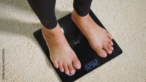 Fotografie Asian young woman leg stepping standing on floor electric scales, female working out at home in living room, female stand on digital weighing machine
