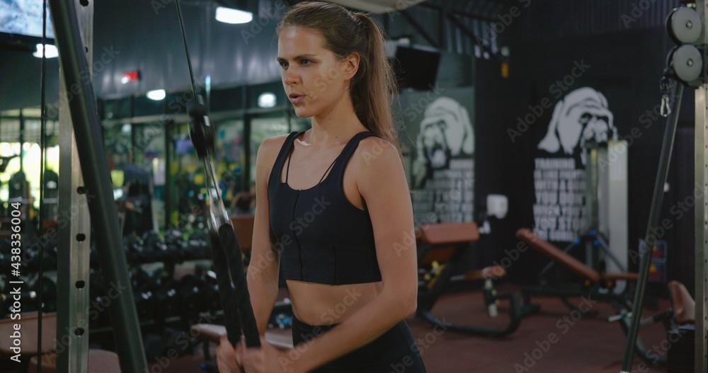 Obraz premium Muscular woman working out exercise for triceps push down weightlifting with pull cable cross machine to flexing muscles at fitness gym, Sport fit workout bodybuilding concept