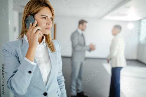 Photo of young worried businesswoman having phone call while standing in hallway before meeting.