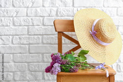 Lilac flowers and hat on chair near brick wall